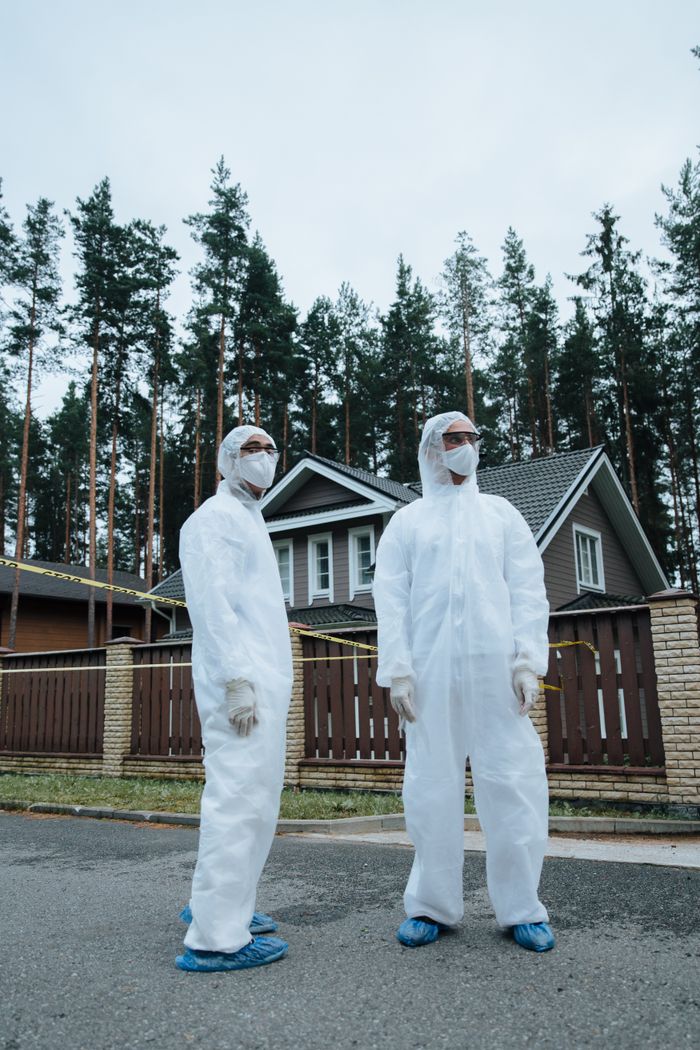 Two healthcare workers in PPE standing outdoors in a residential area.