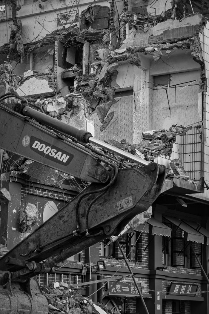 Excavator tearing down urban building, showcasing industrial demolition.