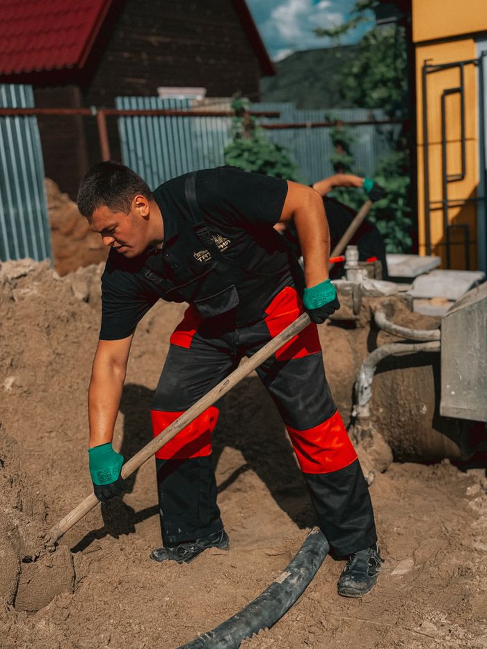 A construction worker in protective gear shoveling sand outdoors at a worksite under sunny conditions.
