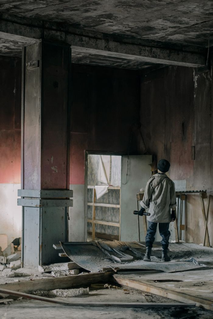 A young man stands alone in a crumbling, abandoned building exploring urban decay.